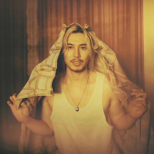 Person with long hair holding a patterned fabric against a warm-toned curtain background